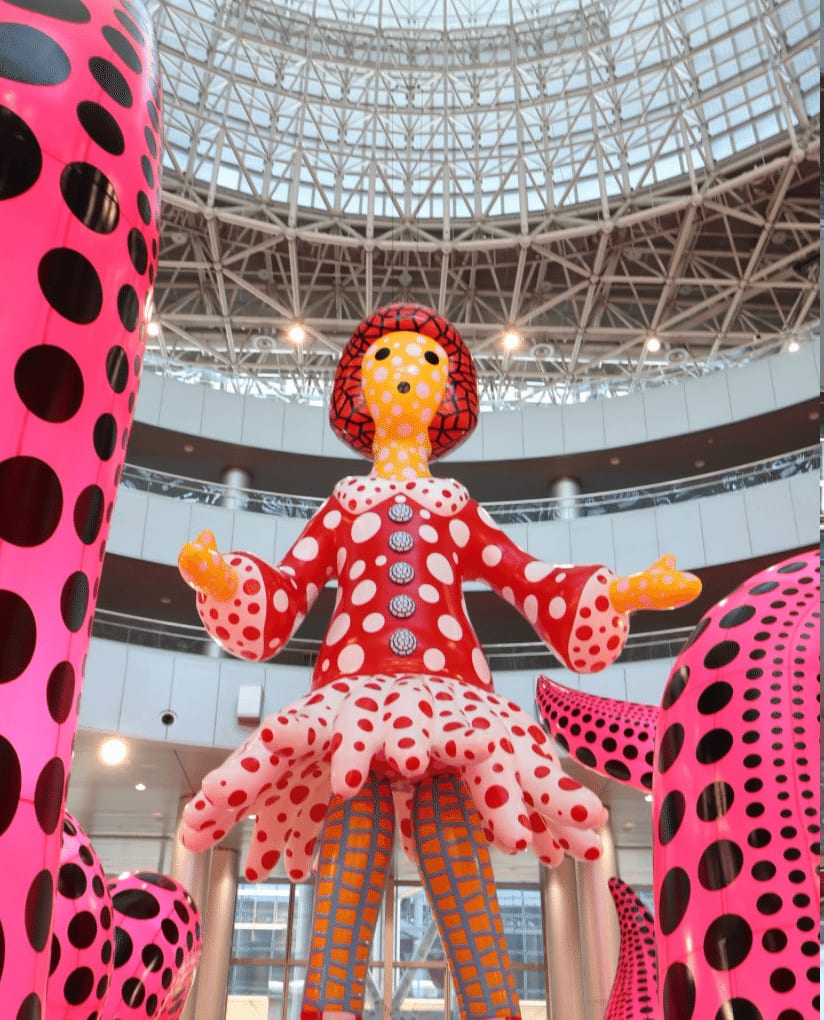 テレコムセンタービルの吹き抜けに立つ、赤い水玉の服を着た大きなバルーン作品《ヤヨイちゃん》